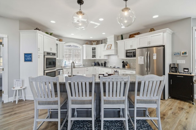 kitchen featuring premium range hood, decorative light fixtures, white cabinets, light stone counters, and black appliances