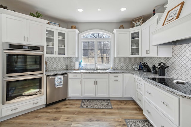 kitchen featuring sink, premium range hood, white cabinetry, appliances with stainless steel finishes, and light stone counters