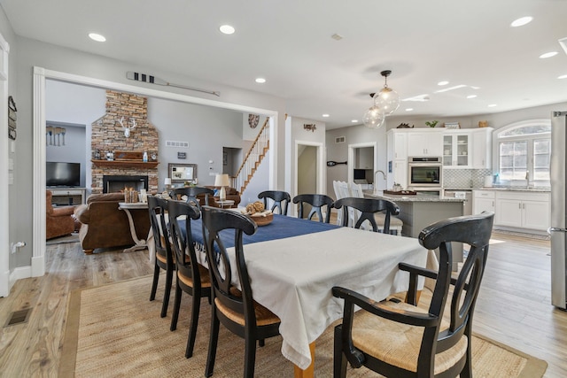 dining area with sink, a stone fireplace, and light hardwood / wood-style floors