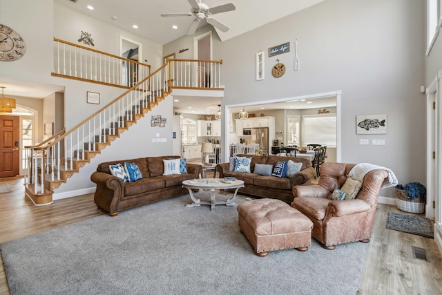 living room featuring wood-type flooring, a towering ceiling, and ceiling fan