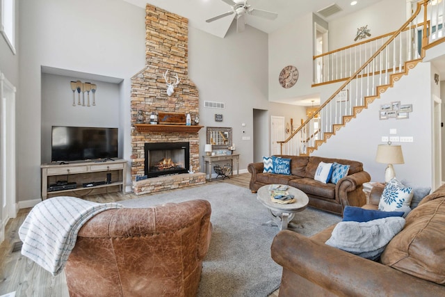 living room with a high ceiling, a stone fireplace, ceiling fan, and hardwood / wood-style flooring