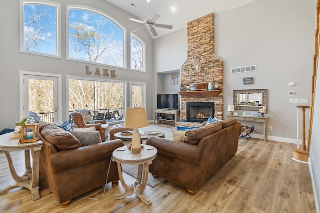 living room featuring ceiling fan, a stone fireplace, high vaulted ceiling, and light hardwood / wood-style floors