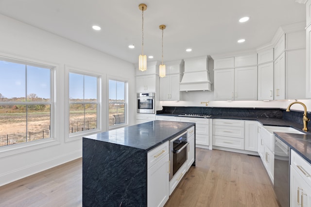 kitchen with sink, appliances with stainless steel finishes, white cabinetry, premium range hood, and a center island