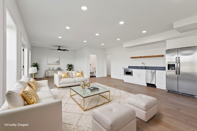 living room with wet bar, ceiling fan, and light wood-type flooring