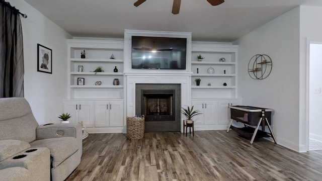 living room with hardwood / wood-style flooring, a large fireplace, ceiling fan, and built in shelves