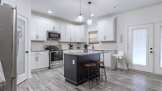 kitchen featuring stainless steel appliances, decorative light fixtures, a kitchen island, and white cabinets