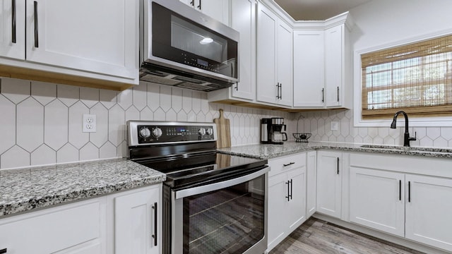 kitchen featuring sink, light stone counters, stainless steel appliances, decorative backsplash, and white cabinets