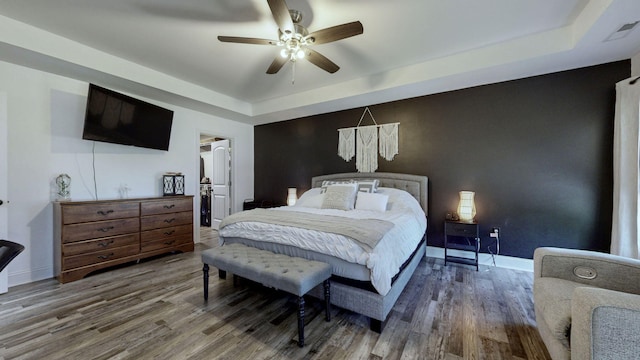 bedroom with hardwood / wood-style flooring, a raised ceiling, and ceiling fan