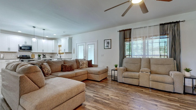 living room with ceiling fan, sink, and light wood-type flooring