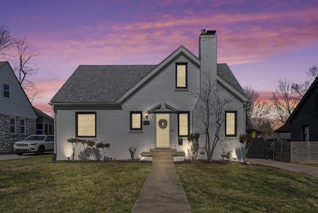 bungalow featuring a front lawn, fence, a shingled roof, brick siding, and a chimney