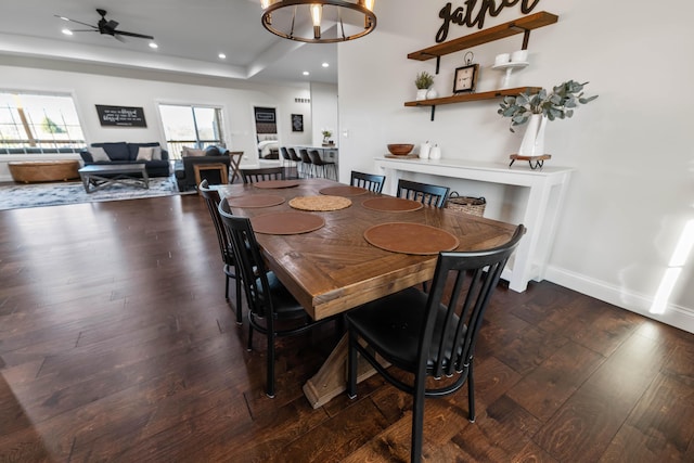 dining room with a tray ceiling, ceiling fan with notable chandelier, and dark hardwood / wood-style floors