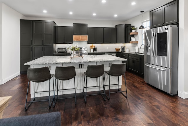 kitchen featuring pendant lighting, a kitchen island, stainless steel appliances, a kitchen bar, and exhaust hood