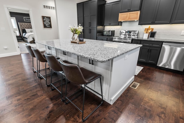 kitchen with extractor fan, appliances with stainless steel finishes, dark hardwood / wood-style floors, a kitchen breakfast bar, and a center island