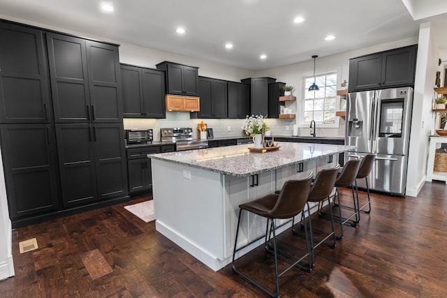 kitchen with decorative light fixtures, sink, a kitchen breakfast bar, light stone counters, and stainless steel appliances