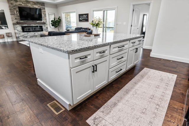 kitchen featuring dark wood-type flooring, light stone counters, a large fireplace, a kitchen island, and white cabinets