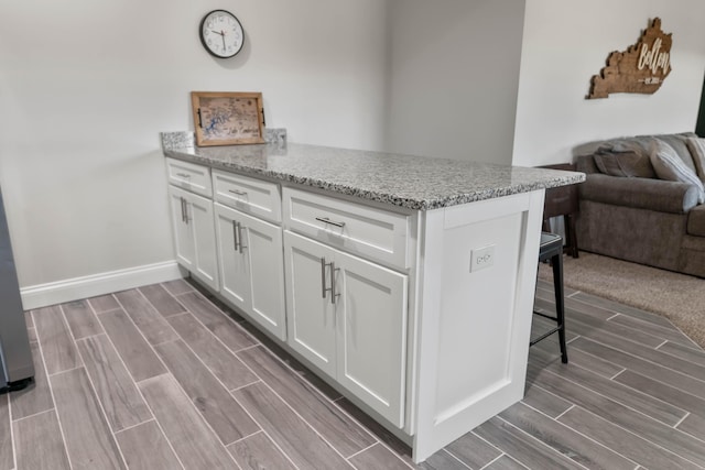 kitchen featuring light stone counters, a breakfast bar area, kitchen peninsula, and white cabinets