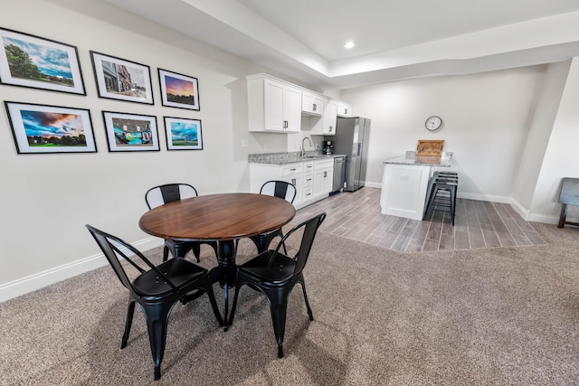 carpeted dining area featuring sink and a raised ceiling