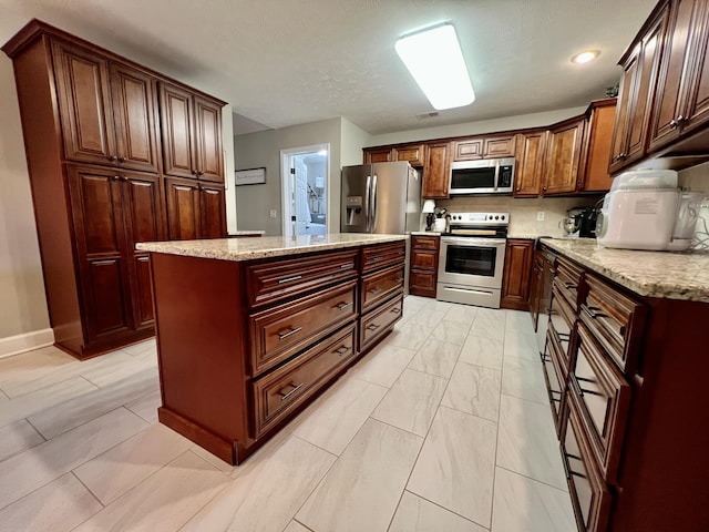 kitchen featuring light stone counters, stainless steel appliances, a center island, and a textured ceiling