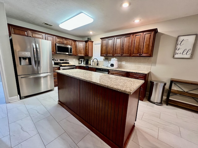 kitchen with light stone counters, decorative backsplash, stainless steel appliances, and a center island