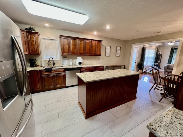 kitchen with sink, stainless steel appliances, a center island, and light stone countertops