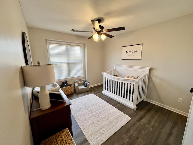 bedroom with a crib, dark hardwood / wood-style floors, and ceiling fan