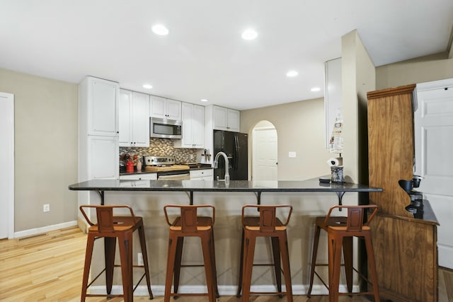 kitchen with tasteful backsplash, white cabinetry, a breakfast bar area, kitchen peninsula, and stainless steel appliances