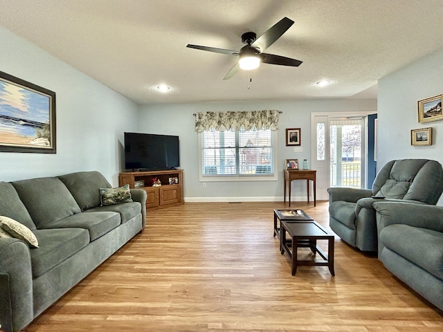 living room with ceiling fan, light hardwood / wood-style flooring, and a textured ceiling