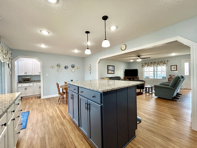 kitchen featuring white cabinetry, light stone countertops, pendant lighting, and light hardwood / wood-style floors