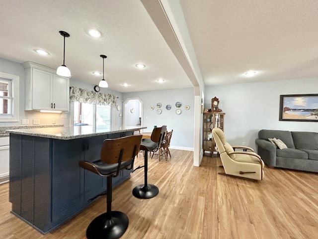 kitchen with a breakfast bar area, white cabinetry, hanging light fixtures, light stone counters, and light hardwood / wood-style floors