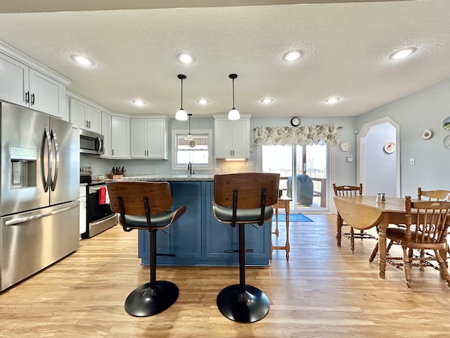 kitchen featuring white cabinetry, a kitchen breakfast bar, hanging light fixtures, light stone counters, and stainless steel appliances