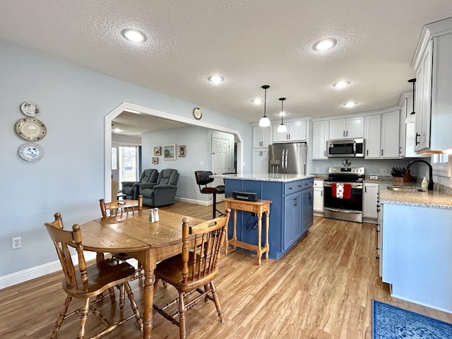 kitchen with pendant lighting, sink, stainless steel appliances, white cabinets, and a kitchen island