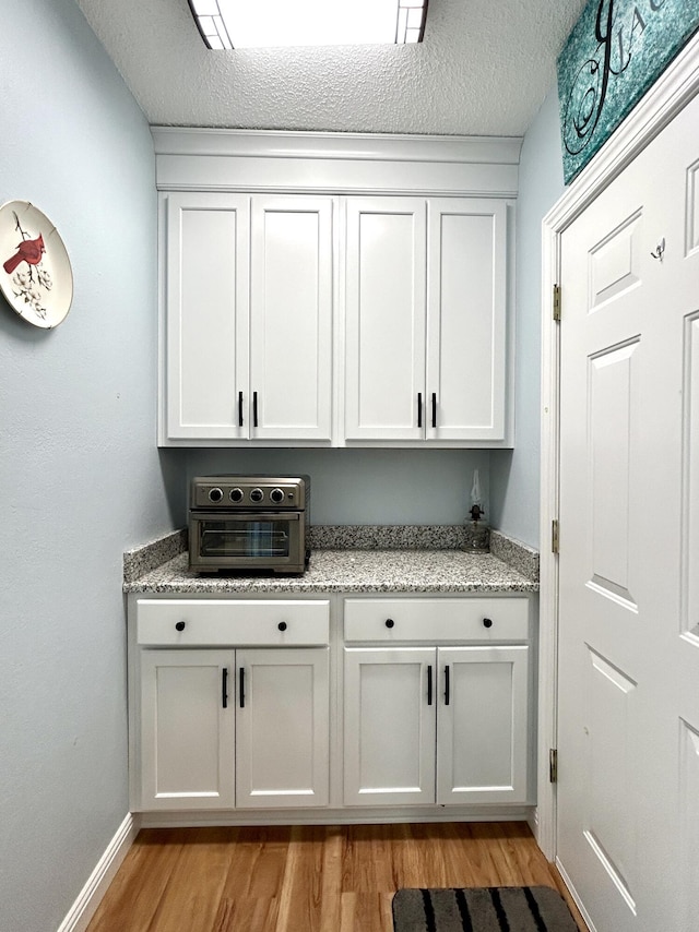 bar featuring a textured ceiling, light stone counters, white cabinets, and light hardwood / wood-style floors