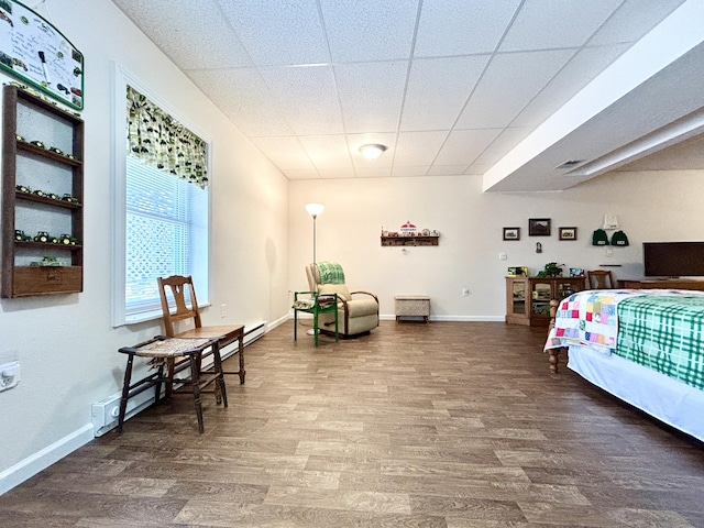 bedroom with dark hardwood / wood-style flooring, baseboard heating, and a drop ceiling