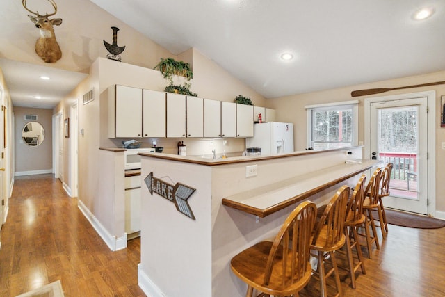 kitchen featuring vaulted ceiling, light wood-type flooring, white cabinets, and white appliances