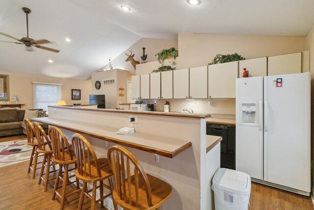 kitchen featuring vaulted ceiling, a breakfast bar, white cabinets, white fridge with ice dispenser, and light hardwood / wood-style floors