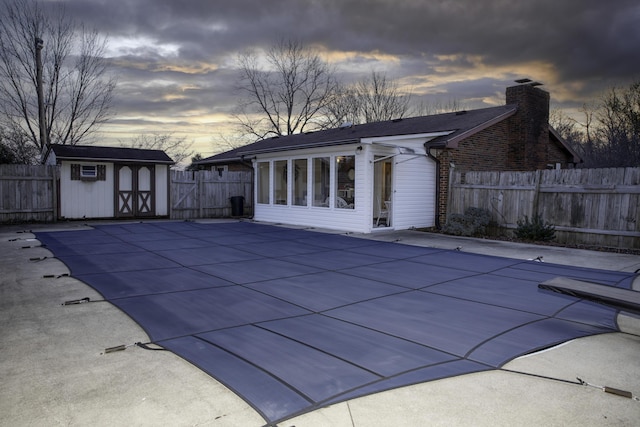 pool at dusk with a storage unit and a patio area