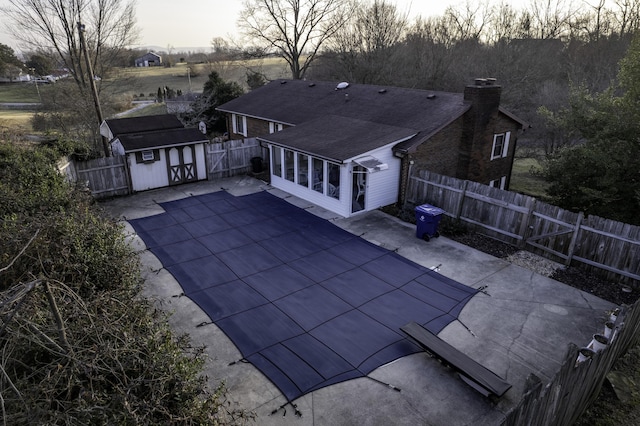 pool at dusk featuring a patio, a grill, and a storage shed