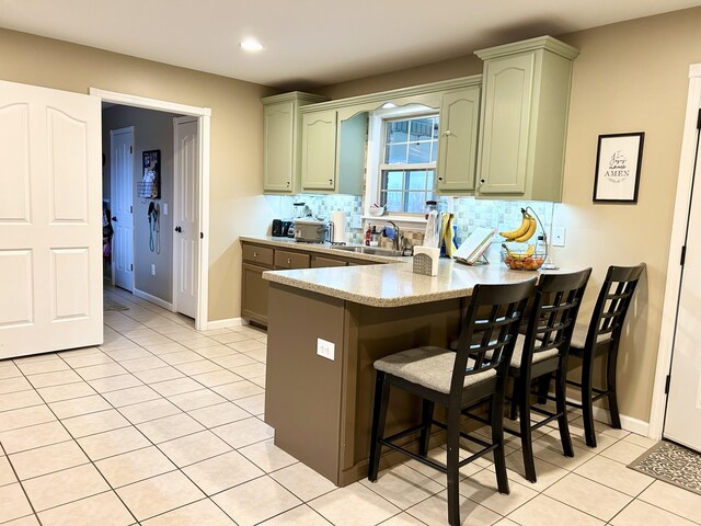 kitchen featuring light tile patterned floors, a breakfast bar area, green cabinets, appliances with stainless steel finishes, and kitchen peninsula