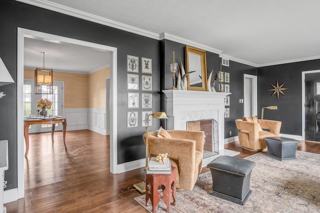 living room with ornamental molding, a high end fireplace, wainscoting, wood finished floors, and baseboards