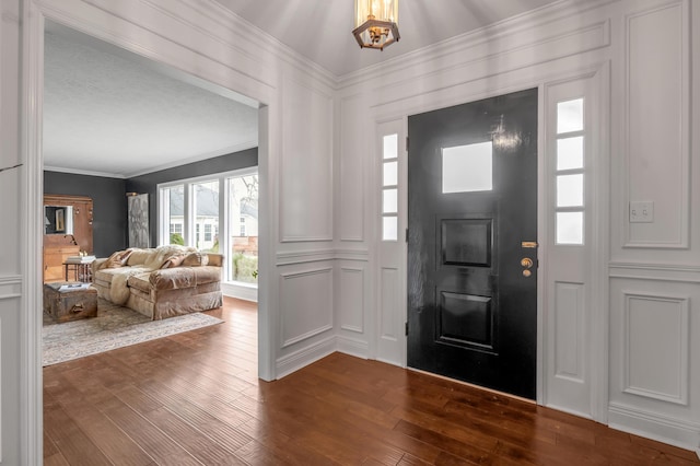 foyer with dark wood-style floors, ornamental molding, and a decorative wall