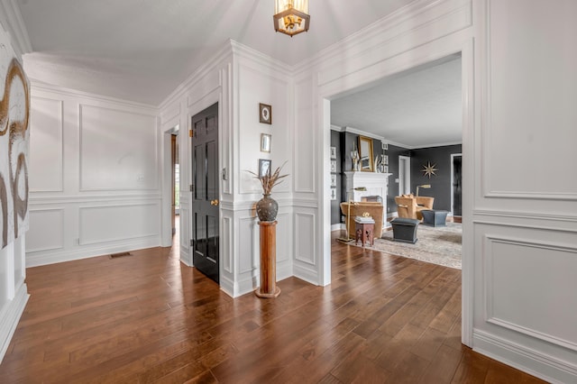 entrance foyer with crown molding, dark wood-style flooring, visible vents, and a decorative wall