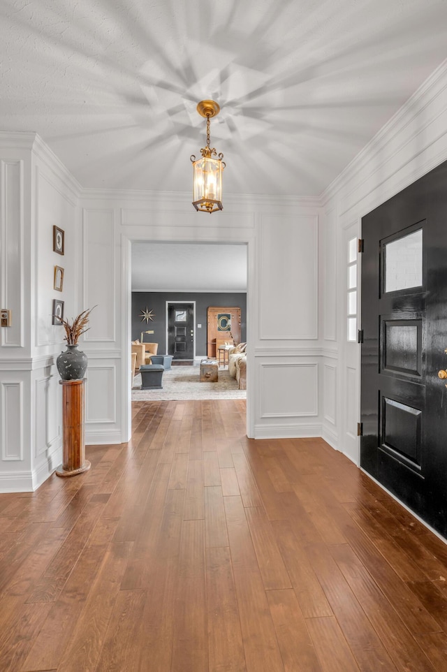 foyer with crown molding, wood-type flooring, an inviting chandelier, and a decorative wall