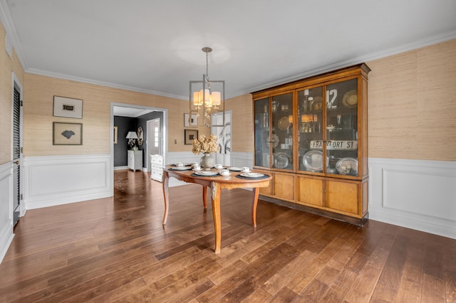 unfurnished dining area with a wainscoted wall, ornamental molding, dark wood-style flooring, and an inviting chandelier