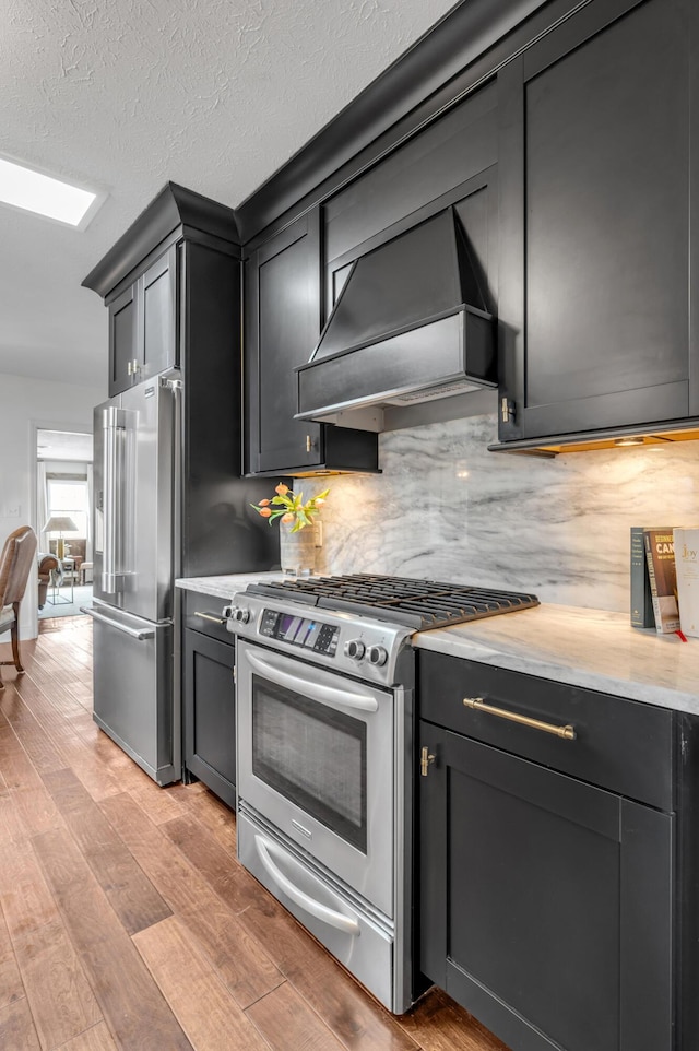 kitchen featuring light wood finished floors, custom range hood, stainless steel appliances, light countertops, and backsplash