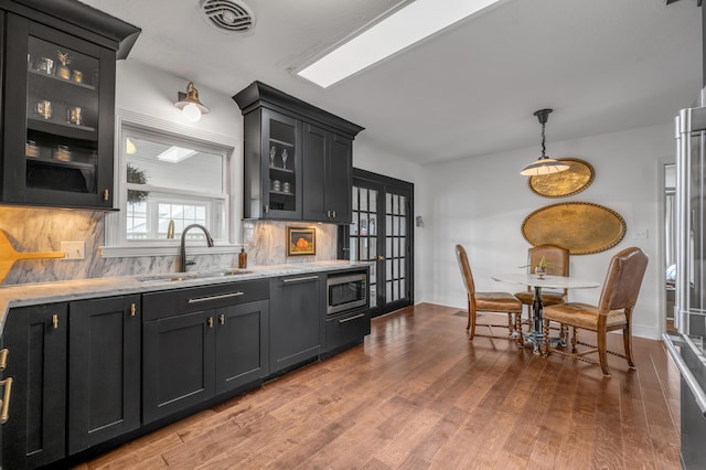 kitchen featuring wood finished floors, a sink, visible vents, tasteful backsplash, and stainless steel microwave