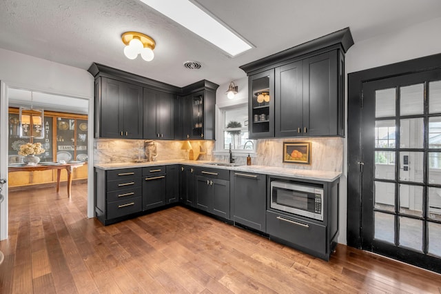 kitchen featuring tasteful backsplash, visible vents, dark wood finished floors, stainless steel microwave, and a sink