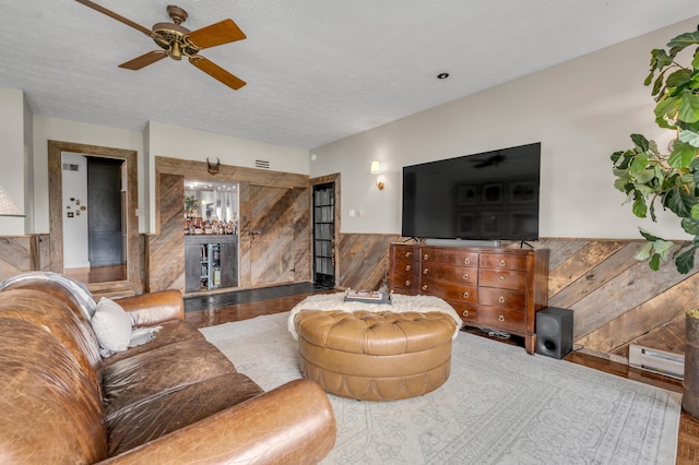 living room with visible vents, a ceiling fan, a textured ceiling, and wainscoting