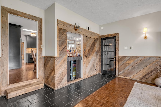 bar featuring a textured ceiling, a bar, wainscoting, and wooden walls