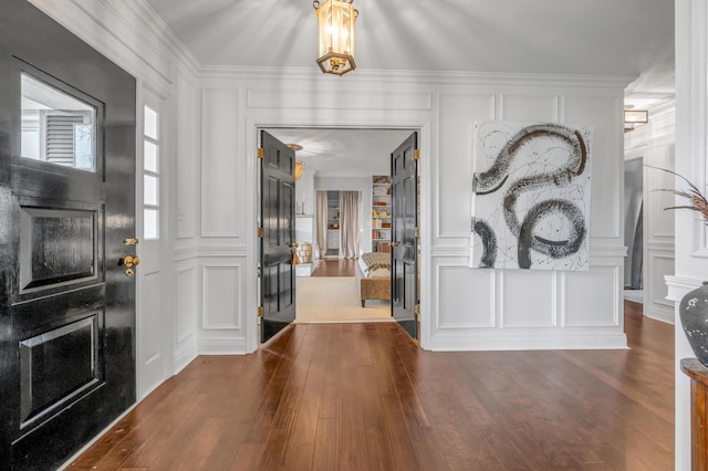 entryway featuring crown molding, dark wood-type flooring, and a decorative wall