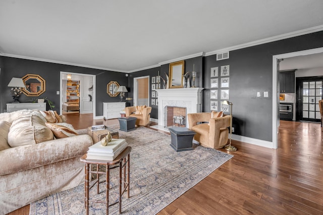 living area featuring baseboards, visible vents, ornamental molding, wood finished floors, and a fireplace